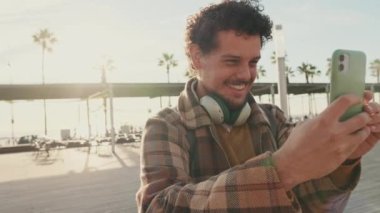 Smiling guy taking a photo on a mobile phone while standing on the street