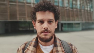 Close up, guy student stands outside the university building looks at the camera and smiles