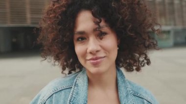 Close up, girl student stands outside the university building looks at the camera and smiles