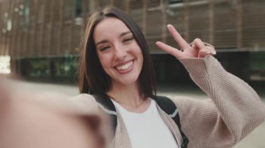 Female student throws up her fingers showing a victory sign shoots on a mobile phone