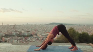 Genç bir kadın gün doğumunda izleme platformunda yoga yapıyor. Amanho mukha svanasana pozu