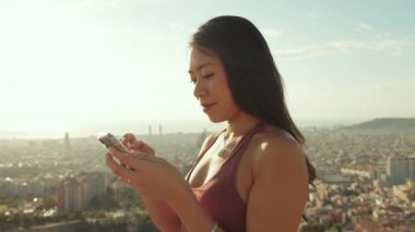 Kapalı, mutlu atletik kadın gözetleme noktasında dururken cep telefonu kullanıyor.