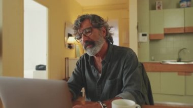 Senier dizüstü bilgisayarda çalışıyor, gözlerini kaldırıyor ve kameraya gülümsüyor.