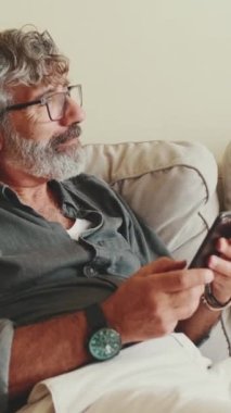 Orta yaşlı bir adam, akıllı telefonuyla mesaj atarken koltuğunda dinleniyor.
