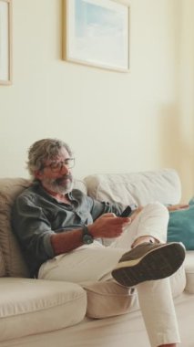 TV uzaktan kumandalı yaşlı bir adam evdeki kanepede oturuyor.