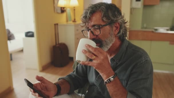 Starší Muž Pečlivě Čte Zprávu Svém Smartphonu Pije Kávu Zatímco — Stock video