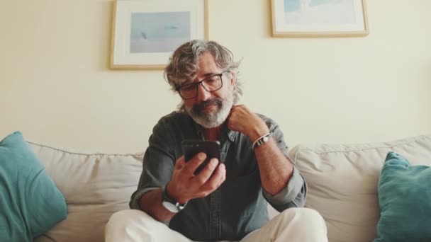 Μεσήλικας Χαλαρώνει Στον Καναπέ Του Ενώ Χρησιμοποιεί Smartphone Του — Αρχείο Βίντεο