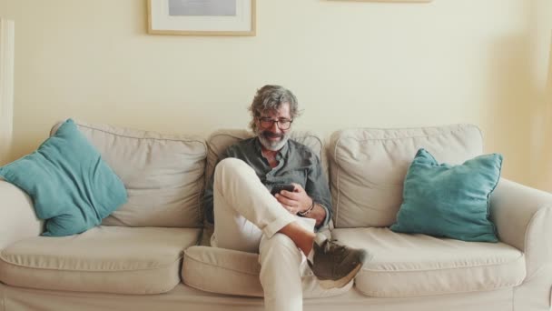 Evde Koltukta Otururken Cep Telefonu Kullanan Yaşlı Pozitif Bir Adam — Stok video