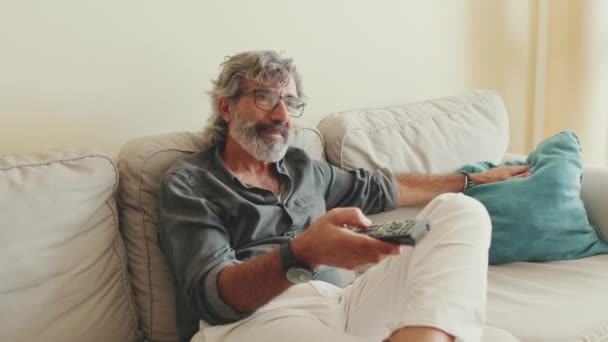 Elderly Man Using Remote Control Switches Channels While Sitting Couch — Vídeo de Stock