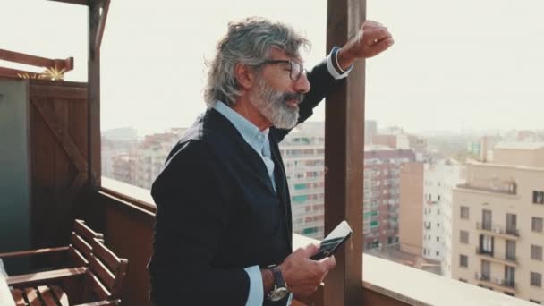 Starší Muž Dívá Městě Balkónu Drží Smartphone Ruce — Stock video
