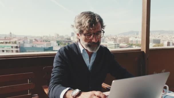 坐在阳台上在笔记本电脑上工作的成熟男人 — 图库视频影像