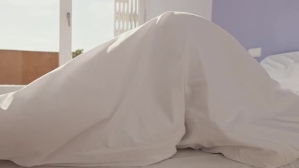 クローズアップ 幸せな女の子のベッドの中でポーズ 女の子は毛布の下から顔をのぞかせ — ストック動画