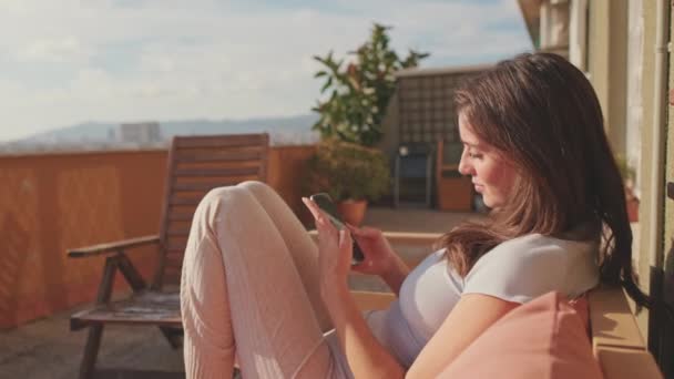 Jonge Vrouw Met Mobiele Telefoon Terwijl Thuis Het Balkon Zit — Stockvideo