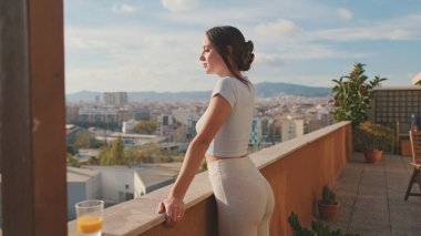 Genç bir kadın balkonda dikilirken güzel manzaranın tadını çıkarıyor.