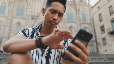 Basamaklardaki genç turist, arka planda otururken cep telefonu kullanıyor