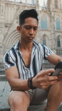 Basamaklardaki genç turist, arka planda otururken cep telefonu kullanıyor