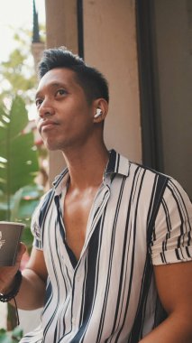 Genç adam dışarıda oturup kahve içiyor.