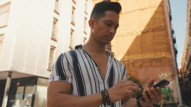 Young man walks along to the road using mobile phone