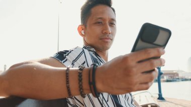 Genç turist iskelede bankta oturuyor ve cep telefonu kullanıyor.. 