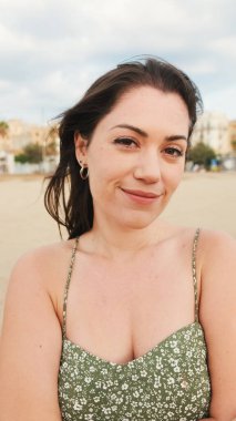 Genç kadın sahilde duruyor ve uzaklara bakıyor. Kız başını çevirir, kameraya bakar ve gülümser.