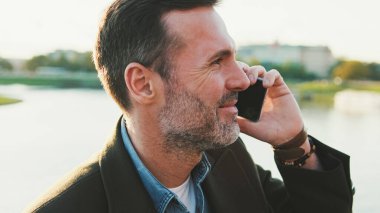 Nehrin kenarında oturan bir adam cep telefonuyla konuşuyor.