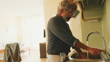 Yaşlı pozitif adam mutfakta sebze yıkıyor.