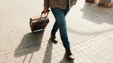 Sokakta bavulla yürüyen orta yaşlı bir adamın bacakları yakın plan.