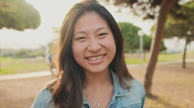 Yaklaş, parkta dururken kameraya poz veren genç kadın. Kameraya bakıyorum.