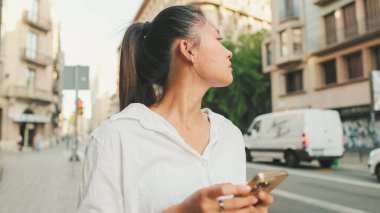 Yolun kenarında dururken cep telefonu kullanan genç bir kadın. Kız etrafına bakıyor.