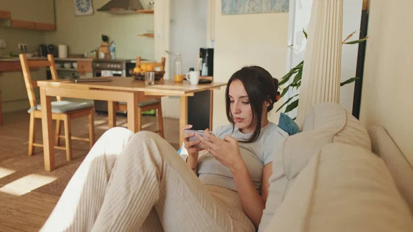 Junge Frau Benutzt Handy Und Wechselt Kanäle Von Der Fernbedienung — Stockfoto