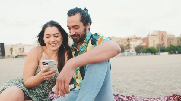 Mladý Pár Používá Mobilní Telefon Zatímco Sedí Pláži Pozadí Budov — Stock fotografie