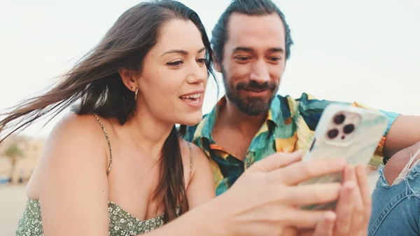 Casal Jovem Usa Telefone Celular Enquanto Sentado Praia Prédios Fundo — Fotografia de Stock