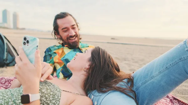 年轻夫妇在海滩上放松 一边聊天 一边用手机 — 图库照片
