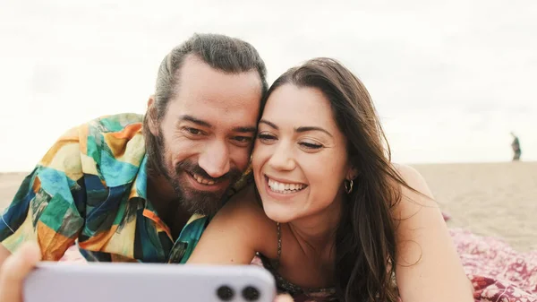 情侣们在沙滩上放松 在手机上看视频和照片 — 图库照片