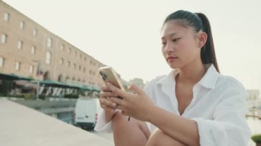 Young woman using mobile phone while sitting in port