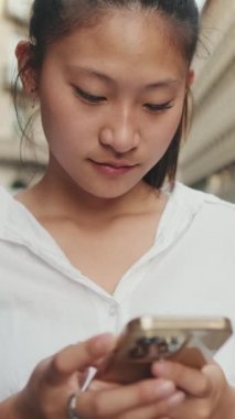 VERTICAL VIDEO: Close up, young woman using mobile phone while standing next to the road