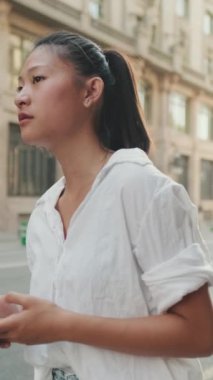 VERTICAL VIDEO: Young woman uses mobile phone while standing next to the road. Girl is waiting for taxi