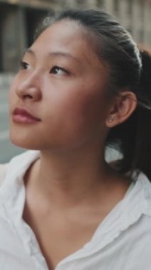 VERTICAL VIDEO: Close up, young woman walks down the street and looks around
