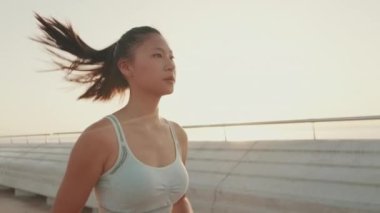 Asian girl in sports top runs along the promenade at morning time