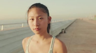 Close up, asian girl in sports top walks along the promenade and looks at the camera