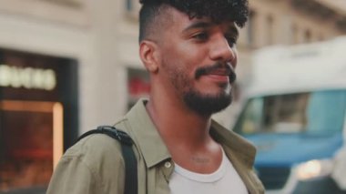 Close up, young smiling man with beard dressed in an olive-colored shirt crosses the road at pedestrian crossing