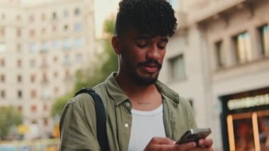 Young happy man with beard dressed in an olive-colored shirt walks through the center of the old city using mobile phone