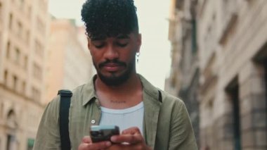 Young smiling man with beard dressed in an olive-colored shirt uses phone on an old city background. Guy reads the good news