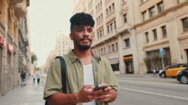 Young happy man with beard dressed in an olive-colored shirt walks through the center of the old city using mobile phone