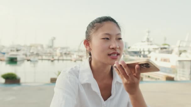 若い女性は海を背景に携帯電話からの音声メッセージを送信します — ストック動画