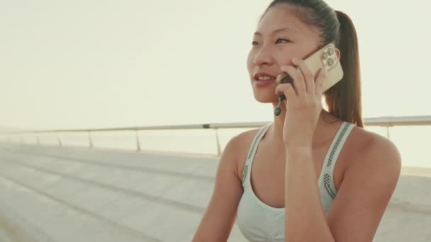 Close Asian Girl Sports Top Sits Embankment Talking Cellphone Camera — Stock video