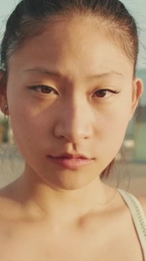 VERTICAL VIDEO: Close up, asian girl in sports top looks at the camera