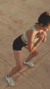 VERTICAL VIDEO: Asian girl in sports top does workout, squats, quadriceps exercises at morning time. View from above