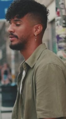 VERTICAL VIDEO: Young man with beard dressed in an olive-colored shirt crosses the road at pedestrian crossing