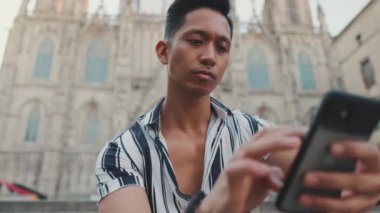 Basamaklardaki genç turist, arka planda otururken cep telefonu kullanıyor